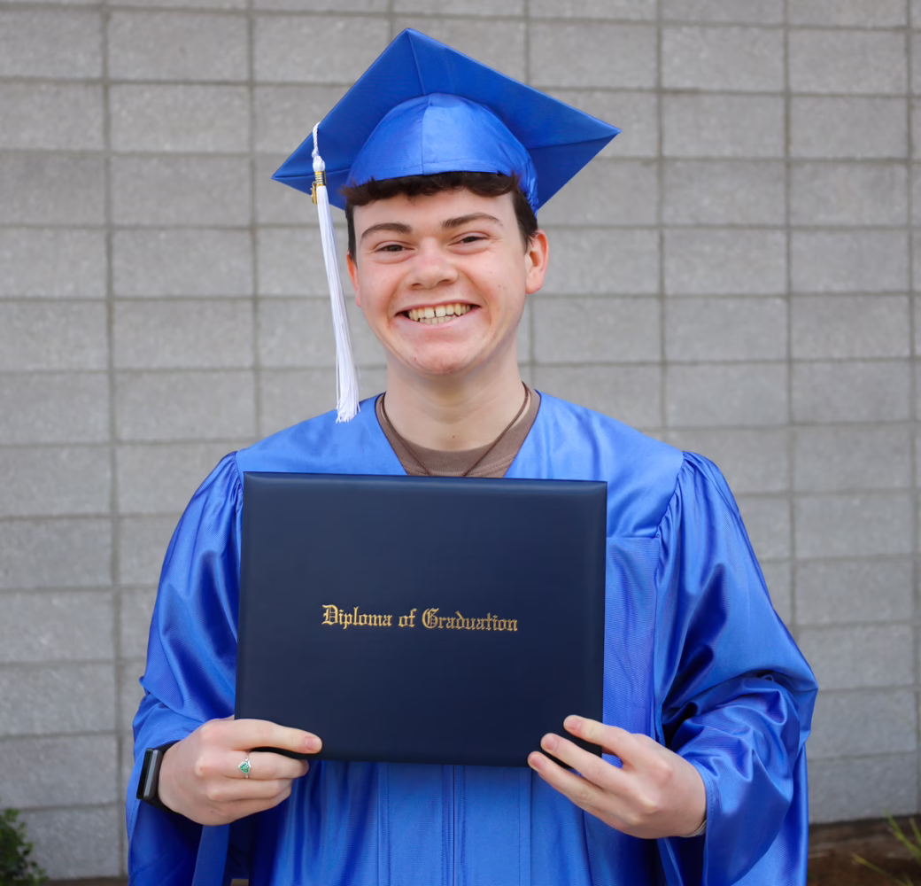 Student smiling while holding their high school diploma