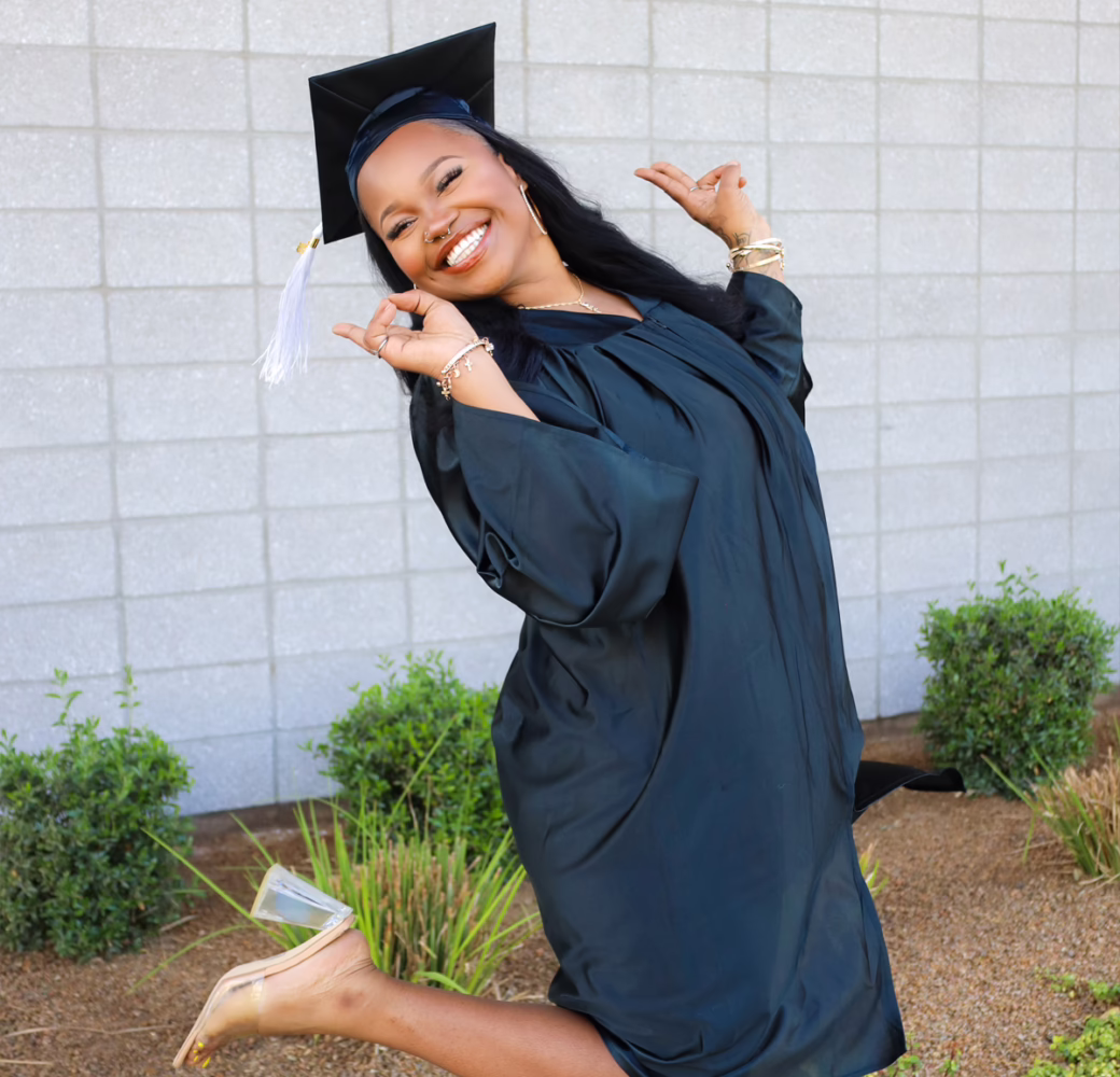 Graduate in a black cap and gown poses outdoors