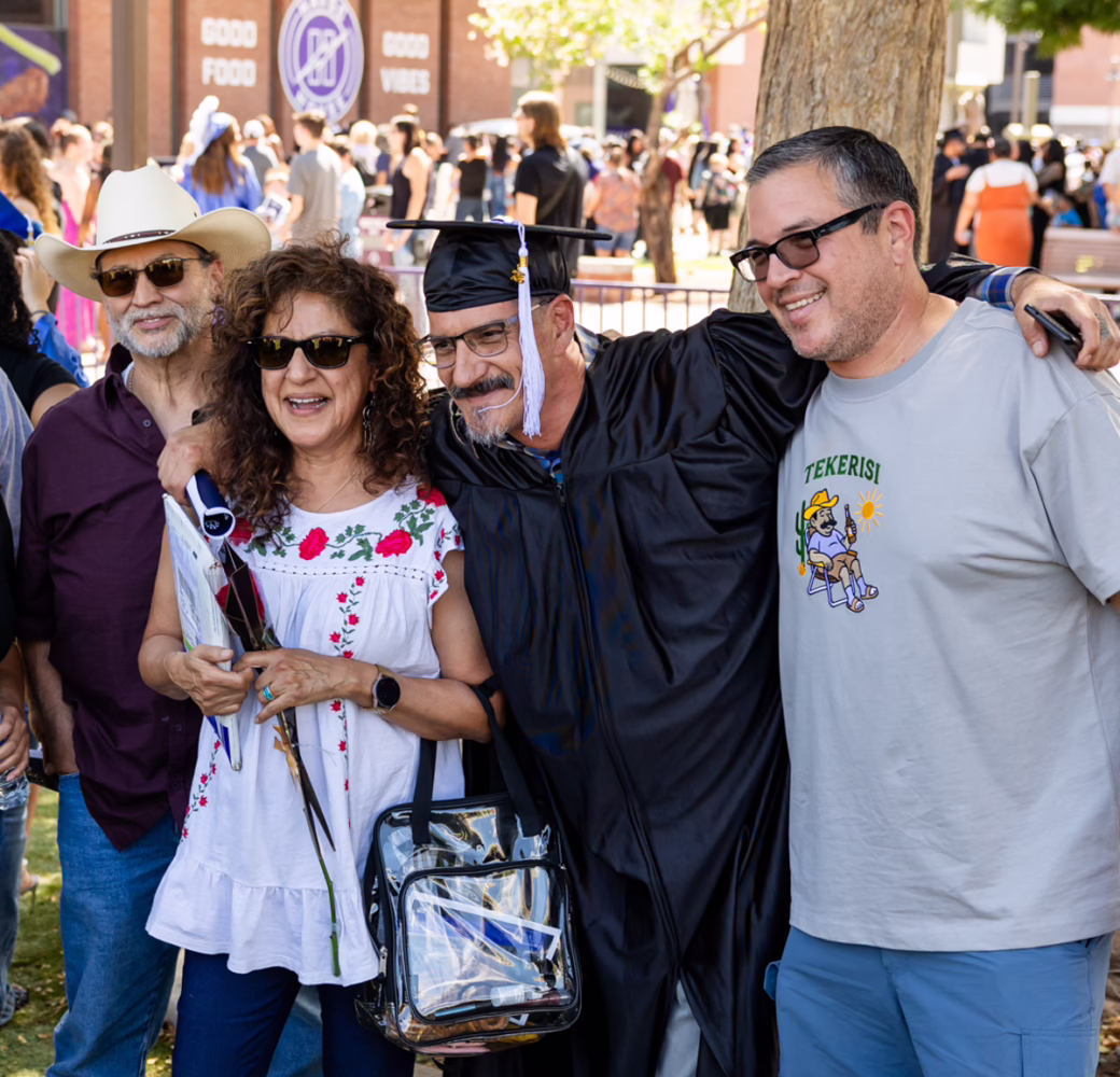 Graduate in a cap and gown poses with family members outdoors following a graduation ceremony.
