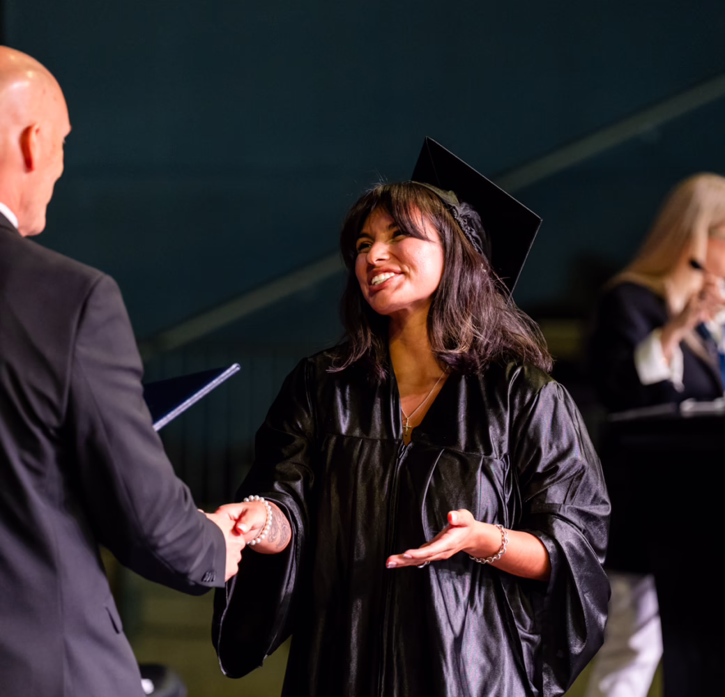 Graduate in cap and gown shaking hands during a graduation ceremony on stage.