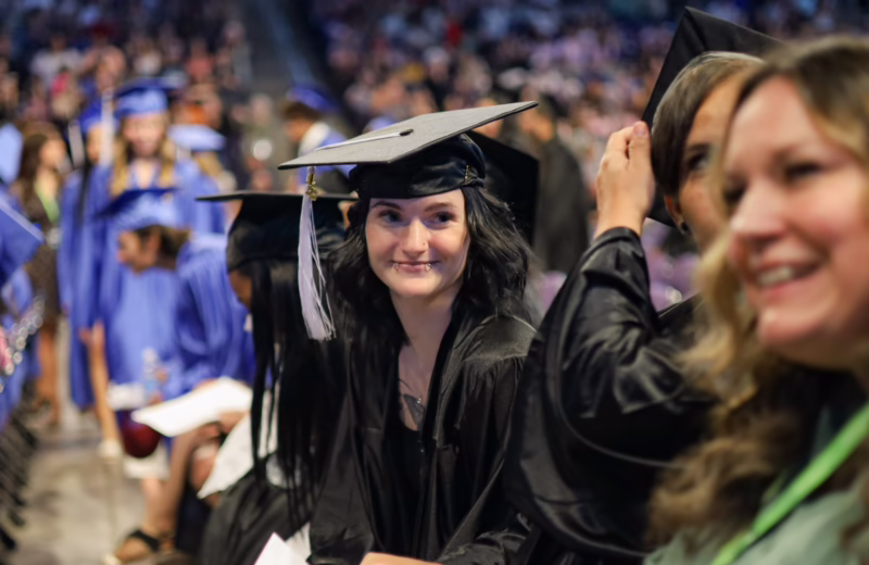 Graduate in a black cap and gown sits among fellow graduates during a commencement ceremony