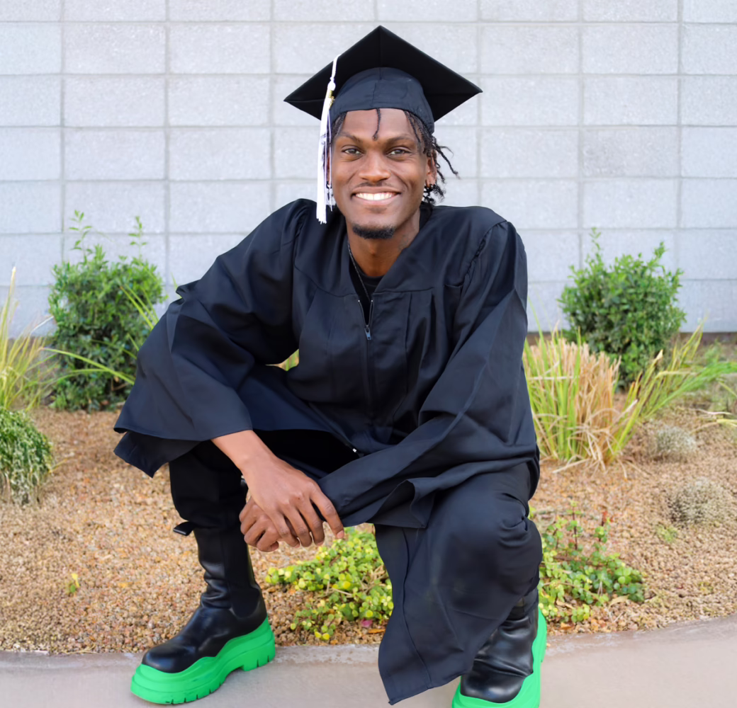 Student wearing a cap and gown kneels and poses before their graduation ceremony