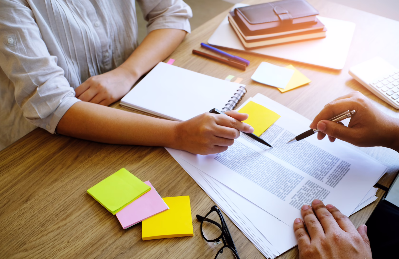 Two people reviewing printed documents at a desk, using pens and sticky notes to discuss and annotate materials.